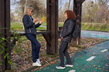 Bir sonbahar parkında gülen ve konuşan iki orta yaşlı kadın arkadaş.