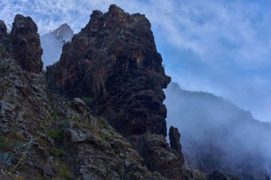 Sivri uçlu Maska kaya oluşumunun dramatik bir görüntüsü. Kısmen kalın beyaz dağ sisi tarafından gizlenmiş..