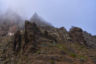 Yanardağ yamacı ve seyrek bitki örtüsü ile sisli Masca kaya oluşumu