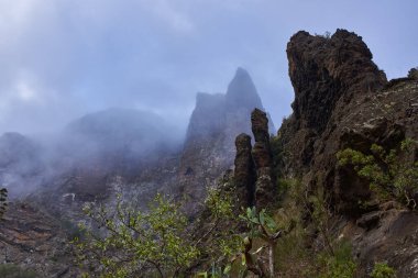Yanardağ yamacı ve seyrek bitki örtüsü ile sisli Masca kaya oluşumu