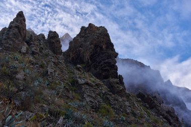 Masca 'nın yükselen volkanik zirvesi yoğun alçak asılı bulutların arasından hızla yükseliyor..
