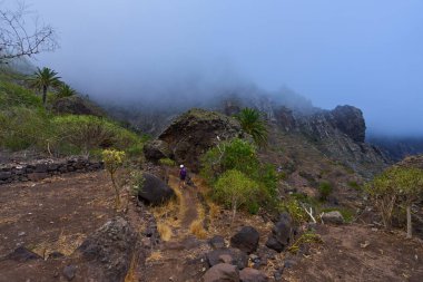 Sisli Masca vadisindeki kadın yürüyüşçü. Arka planda devasa volkanik kayalar ve kayalık oluşumları var.