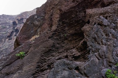 Görünür volkanik katmanlara ve berrak bir gökyüzünün altında keskin tepelere sahip devasa dikey kaya duvarları..