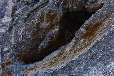 Masca Geçidi 'nin dokulu kaya duvarında katmanlı erozyon desenleriyle karanlık volkanik mağara açılıyor.