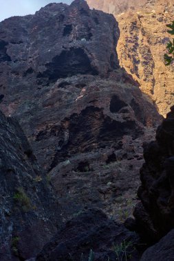 Çoklu volkanik mağara açıkları ve dik Masca geçidi uçurum duvarında seyrek bitki örtüsüyle erozyon desenleri.