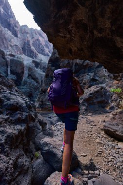 Yürüyüş kasklı ve sırt çantalı bir kadın Tenerifes Masca Vadisi 'nin dik kayalık patikalarında geziniyor..
