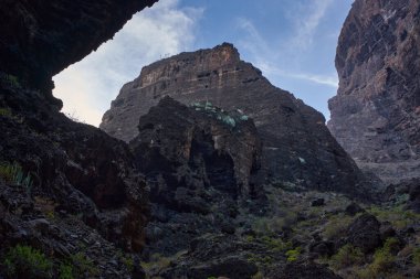 Karanlık mağaranın içinden, yamaçlarda bitki örtüsüyle açılan Masca vadisi uçurum oluşumlarının görüntüsü
