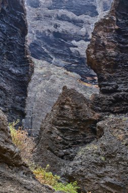 Gündüz vakti birden fazla volkanik mağara açıkları ve dik Masca geçidi uçurum duvarındaki aşınma şekilleri seyrek bitki örtüsüyle birlikte görülüyor.