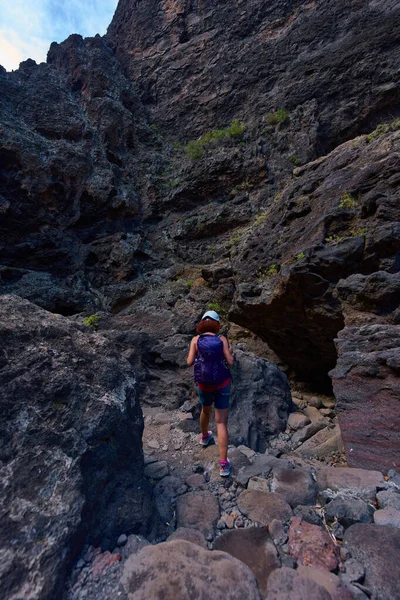Yürüyüş kasklı ve sırt çantalı bir kadın Tenerifes Masca Vadisi 'nin dik kayalık patikalarında geziniyor..