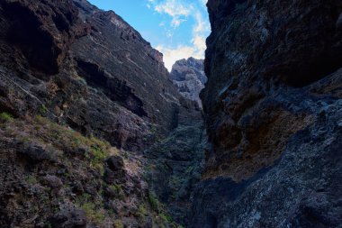 Derin Masca vadisi kanyonundaki mağaraları ve bitkileri olan yüksek volkanik uçurum duvarları boyunca yürüyüş yollarını daraltıyor.