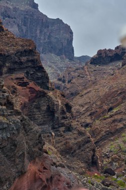 Katmanlı kaya oluşumları mağaralar ve Los Gigantes kayalıklarında seyrek bitki örtüsüyle aşınmış volkanik vadi.