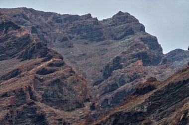 Katmanlı kaya oluşumları mağaralar ve Los Gigantes kayalıklarında seyrek bitki örtüsüyle aşınmış volkanik vadi.