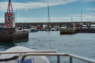 Los Gigantes marinası rıhtıma demirlemiş tekneler ve kanal işaretleriyle dolu bulanık ön planlı tekneden izleniyor.