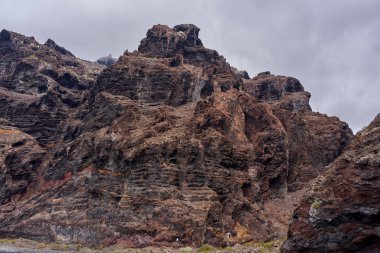 Bulutlu gökyüzünün altındaki Los Gigantes kayalıklarında erozyon desenleri ve renk değişimleriyle katmanlı volkanik kaya oluşumları