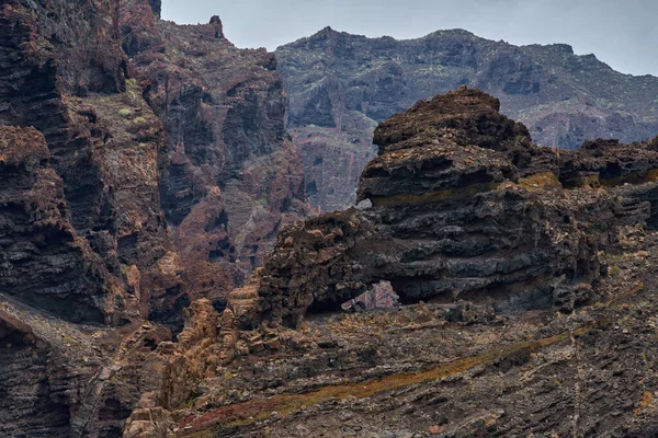 Katmanlı kaya oluşumları mağaralar ve Los Gigantes kayalıklarında seyrek bitki örtüsüyle aşınmış volkanik vadi.