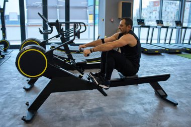 Orta yaşlı bir adam pencereli modern spor salonunda kardiyo çalışması için kürek çekiyor.