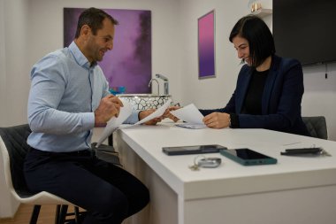 Beyaz ofis masasında gülümseyen kadın ve erkek iş arkadaşları belgeleri gözden geçiriyorlar.