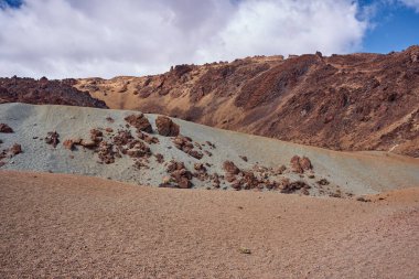 Volkanik sünger taşı sade ve dağınık lav kayaları Tenerife 'deki Teide Ulusal Parkı' nda mavi gökyüzünün altında engebeli bir bazaltik sırtın dibinde.