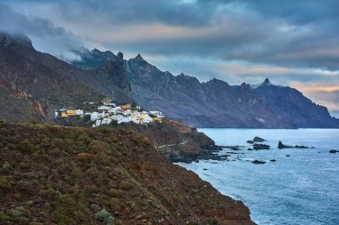 Almaciga köyü Atlantik Okyanusu 'nun yukarısındaki engebeli bir yamaca tünemişti. Tırtıklı Anaga dağ zirveleri ve arka planda dramatik bulutlu gökyüzü vardı.