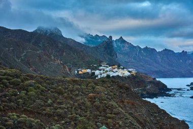 Almaciga köyü Atlantik Okyanusu 'nun yukarısındaki engebeli bir yamaca tünemişti. Tırtıklı Anaga dağ zirveleri ve arka planda dramatik bulutlu gökyüzü vardı.