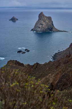 Roque de Dentro ve Roque de Fuera, Roques de Anaga olarak bilinen volkanik monolitler, Tenerife 'nin kuzeydoğu ucundaki Atlantik Okyanusu' ndan yükseliyorlar, bulutlu bir gökyüzü altında yüksek bir kıyı manzarasından görülüyorlar.