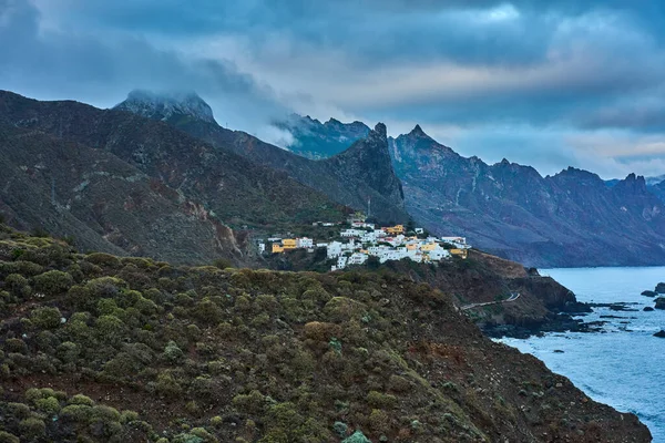 Almaciga köyü Atlantik Okyanusu 'nun yukarısındaki engebeli bir yamaca tünemişti. Tırtıklı Anaga dağ zirveleri ve arka planda dramatik bulutlu gökyüzü vardı.