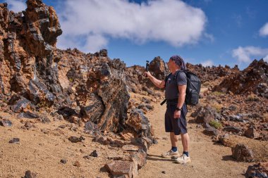 Sırt çantalı bir erkek yürüyüşçü Tenerife, Teide platosundaki Minas de San Jose 'de obsidiyen volkanik bir kaya oluşumunu filme alır.