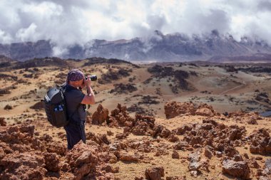 Sırt çantalı bir erkek fotoğrafçı Minas de San Jose 'deki yüksek kayalık bir noktadan yayılan volkanik platoyu sünger taşı tepecikleri ve bulutlarla kaplı dağlarla Tenerife' ye doğru uzanan