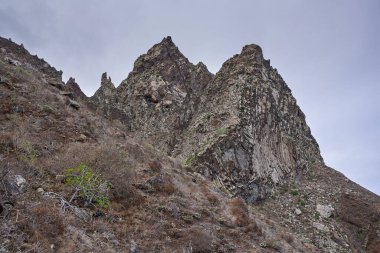 Tırtıklı volkanik kayalıklar ve dik uçurumlar Tenerife 'nin Anaga dağlarındaki kuru bir ovanın tepesinde, bulutlu bir gökyüzünün altında yükseliyor.
