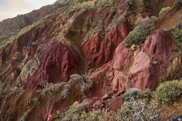 Tenerife 'nin Anaga Dağları' ndaki dik bir vadide bulunan kırmızı ve koyu volkanik kaya oluşumları seyrek çalılık bitki örtüsüyle