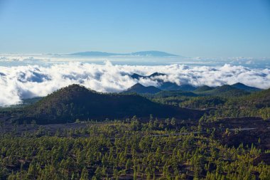 Samara volkanından gündüz görüşü çam ormanlarıyla kaplı volkanik tepeler ve La Palma adası ile birlikte bir bulut denizi.