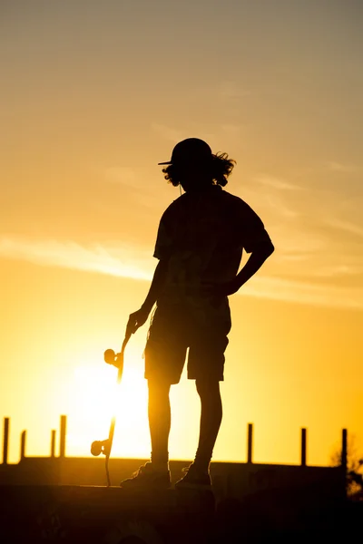 Teen boy silhouette with skateboard at sunset — Stock Photo, Image