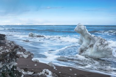 Pasifik Okyanusu 'nun güzel kış güneşli manzarası. Dalgaları yıkayan siyah volkanik kum ve buz blokları. Kamçatka, Rusya.