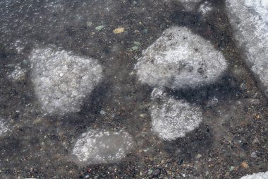 Donmuş bir körfezin yüzeyinde eriyen buzla birlikte bahar arkaplanı. Donmuş bir gölün karlı kıyısı.