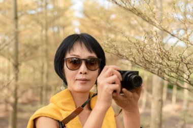 Modern Asyalı kadın ormanda bir kamera tutuyor.