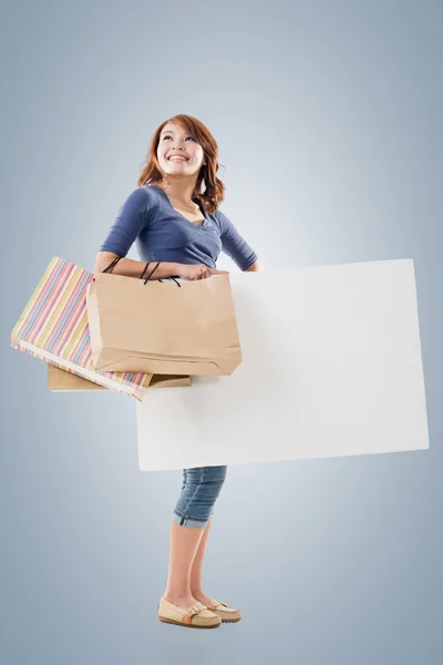 Shopping kvinna anläggning väskor och Tom styrelse — Stockfoto