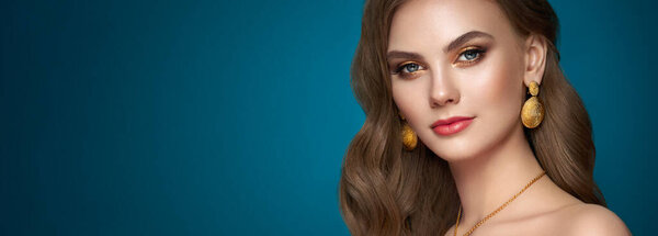 Brunette girl with perfect makeup. Beautiful model woman with curly hairstyle. Care and beauty hair products. Lady with fashionable gold makeup. Model with jewelry on dark blue background