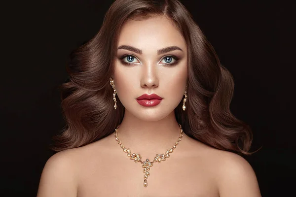 Brunette Girl with Long and shiny Curly Hair. Beautiful Model Woman with Curly Hairstyle. Care and Beauty Hair products. Perfect Make-Up and Jewelry