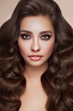 Mükemmel makyajlı esmer kız. Uzun kıvırcık saçlı, gülümseyen güzel model kadın. Bakım ve güzellik saç ürünleri