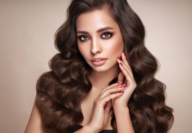 Mükemmel makyajlı esmer kız. Uzun kıvırcık saçlı, gülümseyen güzel model kadın. Bakım ve güzellik ürünleri. Kırmızı tırnaklı manikür.