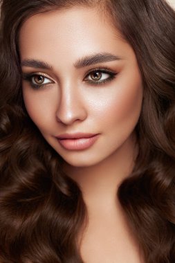 Mükemmel makyajlı esmer kız. Uzun kıvırcık saçlı, gülümseyen güzel model kadın. Bakım ve güzellik ürünleri. Mavi elbiseli model