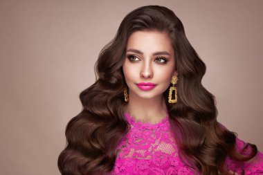 Mükemmel makyajlı esmer kız. Uzun kıvırcık saçlı, gülümseyen güzel model kadın. Bakım ve güzellik ürünleri. Pembe elbiseli bir model.