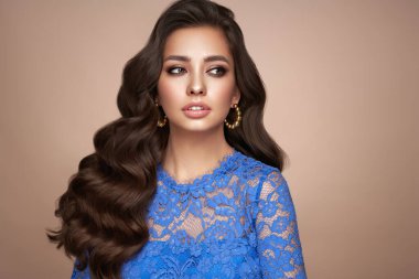 Mükemmel makyajlı esmer kız. Uzun kıvırcık saçlı, gülümseyen güzel model kadın. Bakım ve güzellik ürünleri. Mavi elbiseli model