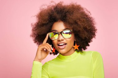 Renkli holografik güneş gözlüklü Afrikalı Amerikalı kızın güzel portresi. Pembe arka planda güzel siyah bir kadın. Kozmetik, makyaj ve moda