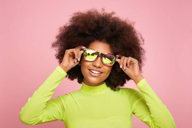 Renkli holografik güneş gözlüklü Afrikalı Amerikalı kızın güzel portresi. Pembe arka planda güzel siyah bir kadın. Kozmetik, makyaj ve moda