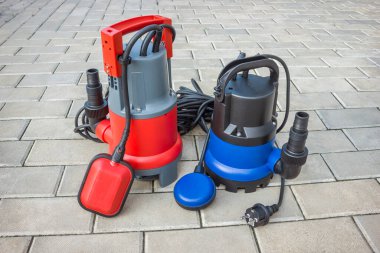 Avlunun taş zemininde plastik evleri olan iki ev içi su altı pompası.