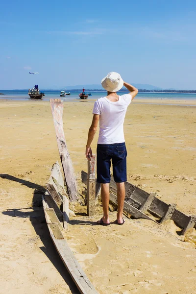 Молодой незнакомец сидит на разбитой лодке — стоковое фото
