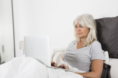 Orta yaş kadın yatakta bir dizüstü bilgisayar ile