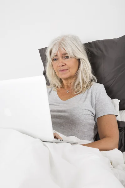 Donna di mezza età con un computer portatile a letto — Foto Stock