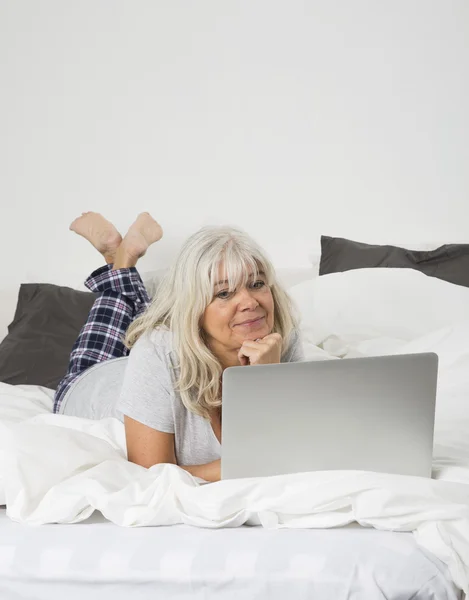 Mid Age woman with a laptop in bed — Stock Photo, Image